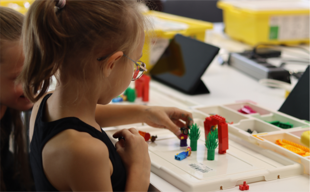 Kleines Mädchen sitzt am Tisch und spielt LEGO